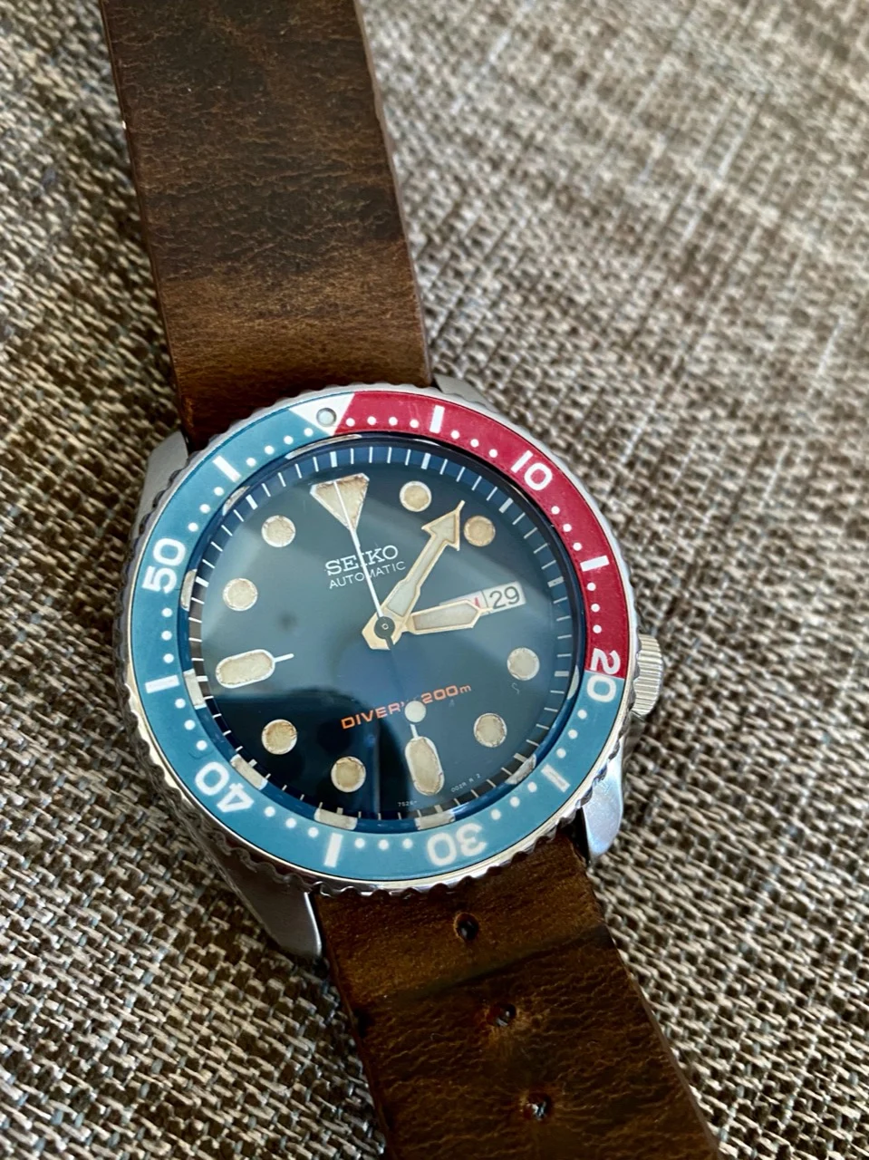 A customized Seiko dive watch with a faded red-and-blue bezel, aged dial, and brown leather strap