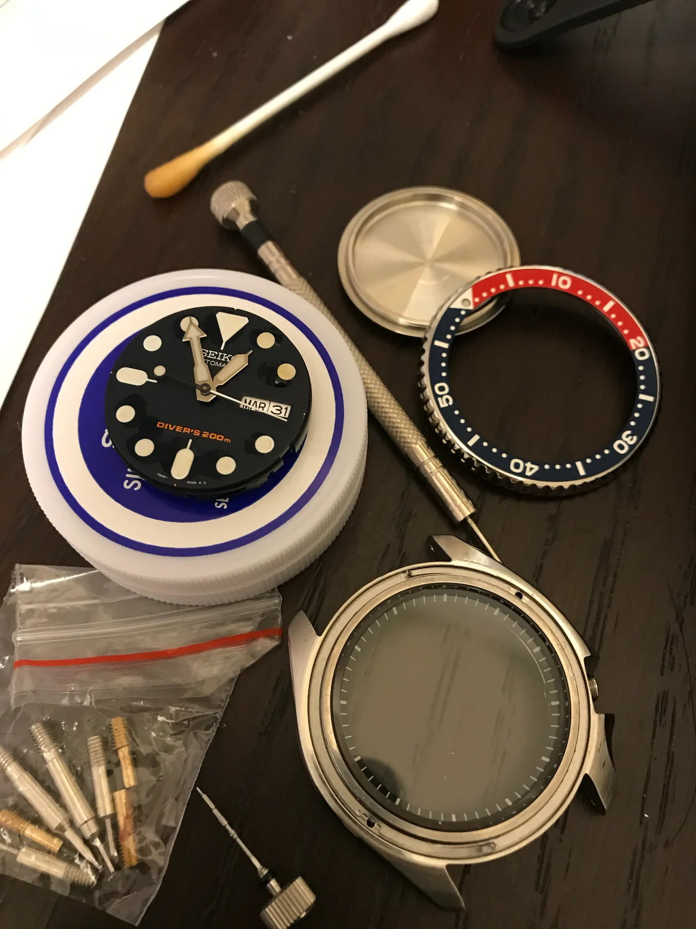 A Seiko watch dial, bezel, case, and watchmaking tools arranged during modification