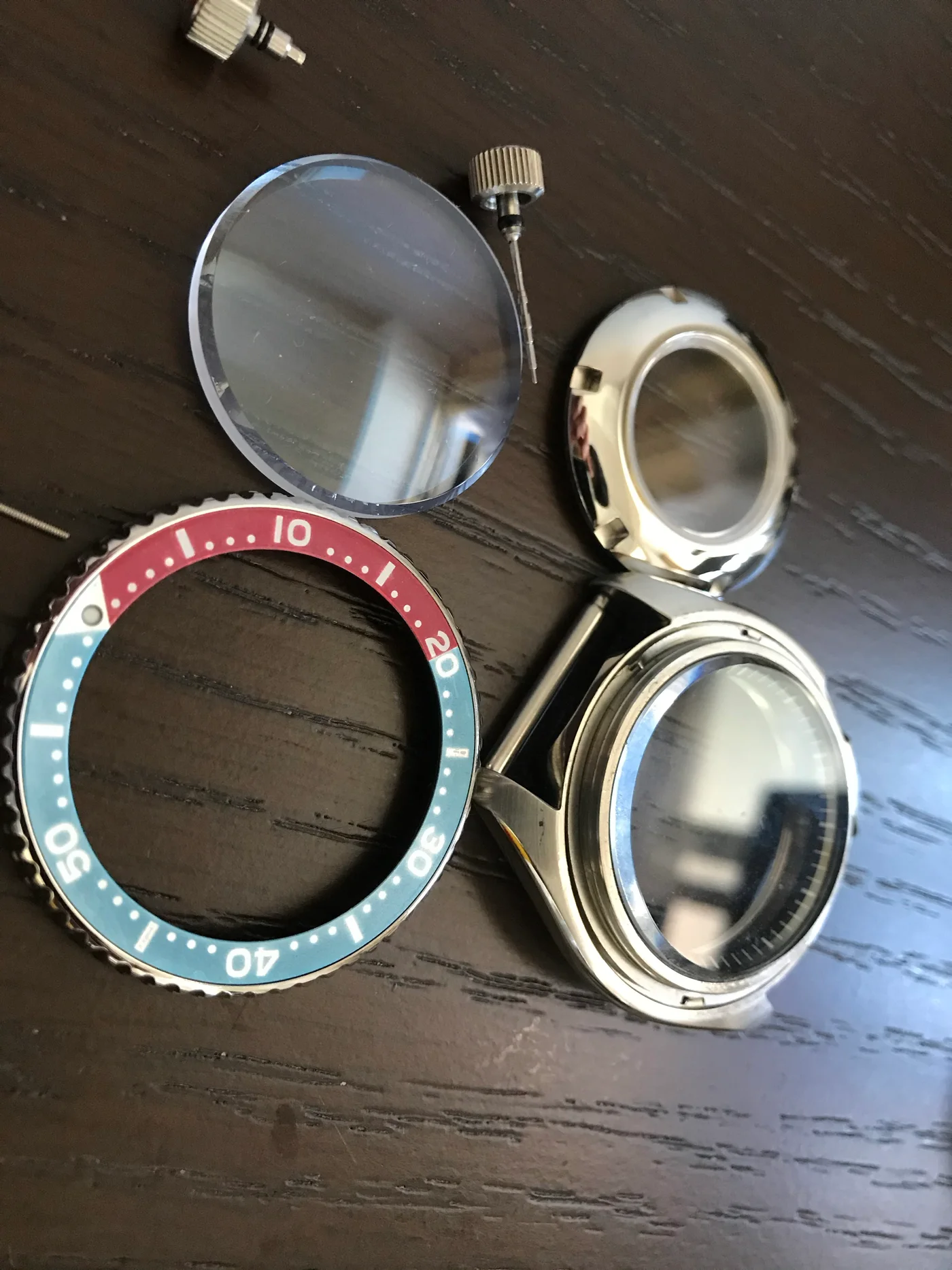Watch cases, crystal, bezel, stems, and crowns disassembled on a work surface